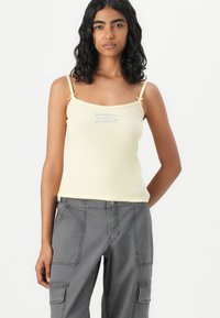 Yellow ribbed tank top with thin straps and a loop detail on the shoulders. Features a small blue embroidered design on the front.