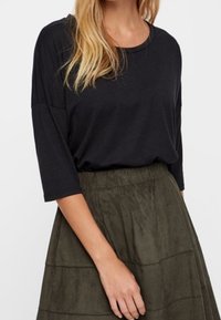 Černý, volnější top se třičtvrtinovými rukávy, zkombinovaný s texturovanou olivově zelenou sukní s vodorovnými patry a elastickým pasem.