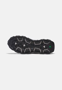 Suela de zapato de goma negra con surcos profundos, que presenta patrones triangulares y hexagonales, un acento verde y una superficie texturizada para mayor agarre.