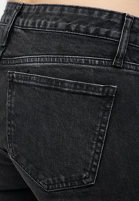 Λεπτομέρεια πίσω τσέπης μαύρου ξεθωριασμένου τζιν με ραφές, θηλιά για ζώνη και υφή υφάσματος.