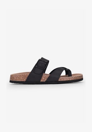 Black sandal with cork midsole, featuring a wide strap with a buckle and crossed toe straps. Flat sole design with rubber bottom.