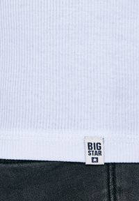 Fehér bordázott szövet, felette egy kis "BIG STAR" címke, az alsó szélén sötét farmeranyag.