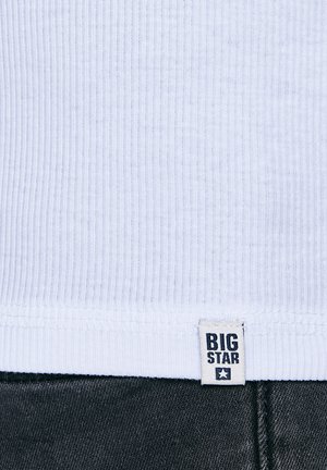 Fehér bordázott szövet, felette egy kis "BIG STAR" címke, az alsó szélén sötét farmeranyag.