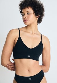 Zwarte geribbelde bralette met dunne verstelbare bandjes en een V-halslijn, met een klein wit "HUGO" logo op de band.