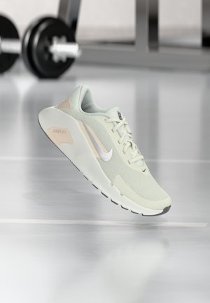 Zapatilla de correr Nike verde claro con el logo blanco de Nike swoosh, mostrada en un gimnasio con pesas desenfocadas al fondo.