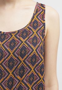 Débardeur sans manches avec un motif en diamant dans des teintes de bleu foncé, jaune, rose et rouge. Fabriqué en tissu léger avec une finition texturée.