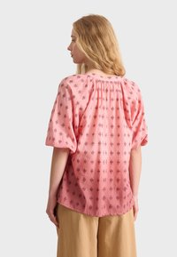 Blusa rosa con una vestibilità comoda, maniche a sbuffo e dettaglio arricciato sul retro, caratterizzata da un motivo floreale in rosa scuro e accenti blu navy.