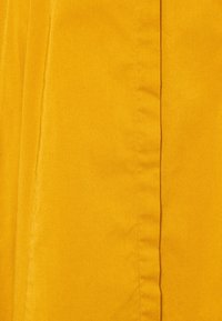 Żółta tkanina o gładkiej fakturze, z widocznymi szwami i lekko błyszczącym wykończeniem. Materiał wydaje się lekki i trwały.