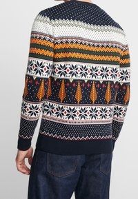 Stickad tröja i marinblått med flerfärgade geometriska mönster inklusive träd, snöflingor och zickzackar. Ribbstickade manschetter och nederkant.