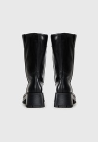 Bottes noires en cuir montantes avec un talon épais et texturé. Finition lisse, bout arrondi et design minimaliste pour un look contemporain.