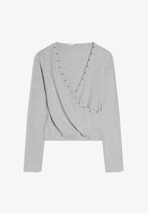 Világosszürke hosszú ujjú átlapolt felső V-nyakkivágással, apró kerek fém szegecsekkel díszítve a nyakkivágás és az elülső él mentén.
