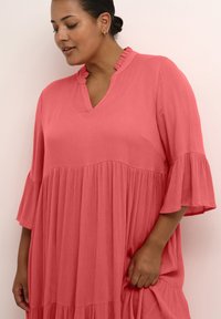 Vestido coral rosa con escote en V, cuello con volantes y mangas cortas acampanadas. Presenta un diseño en capas con tejido texturizado y un corte holgado.