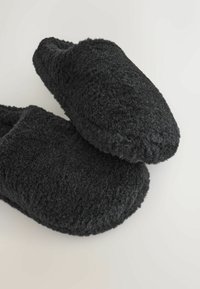 Papuci din lână neagră cu o suprafață texturată, vârf rotunjit și căptușeală moale. Designul este tip slip-on, oferind confort și căldură.