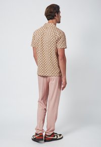 Camisa de manga corta con un patrón geométrico en amarillo, rojo y púrpura. Combinada con pantalones ajustados rosa claro y zapatillas multicolor.