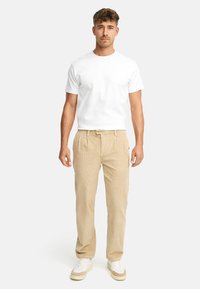 White short-sleeve t-shirt, beige corduroy pants, and white sneakers with tan accents. Model stands upright against a plain background.