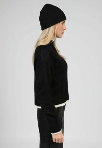 Pull en maille noire avec un col montant, design court avec une bordure blanche à l'ourlet et aux poignets. Associé à un bonnet côtelé noir.