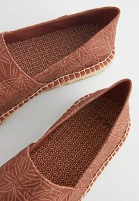 Červené plátené espadrilky s motívom listov, tkanou jútovou podošvou a kontrastným prešitím pozdĺž okraja. Interiér má geometrický vzor.