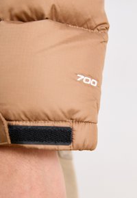 Barna puffjacke ujján steppelt textúra, fehér "700" hímezés és fekete tépőzáras rögzítő.