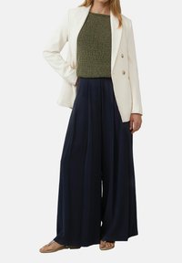 Witte op maat gemaakte blazer, groene gestructureerde gebreide top, marineblauwe wijde broek en tan sandalen. Soepele stoffen met gestructureerde ontwerpelementen.