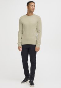 Jasnozielony sweter dziany z długim rękawem, okrągłym dekoltem i ściągaczami na rękawach, w zestawieniu z czarnymi spodniami slim-fit i czarnymi trampkami.