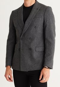Grijze wollen blazer met een dubbelgeknoopt ontwerp, ingesneden revers en twee voorzakken. De stof heeft een zachte, gestructureerde uitstraling.