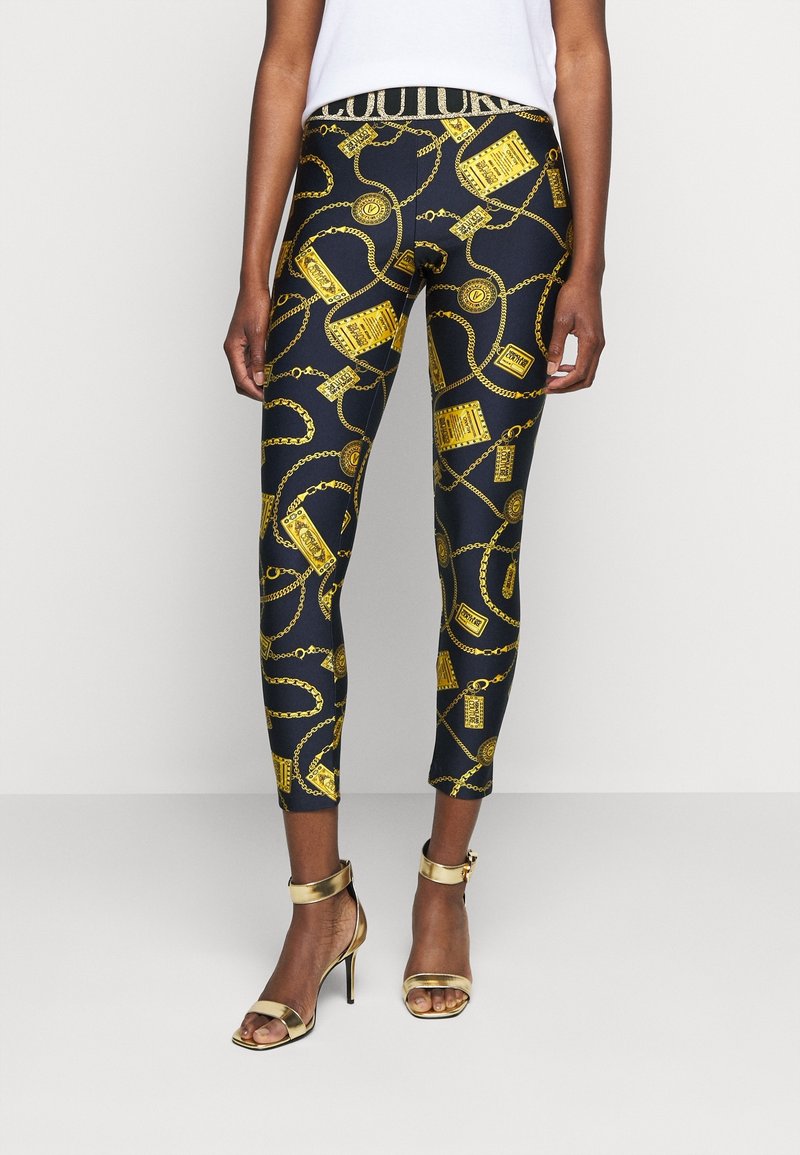 Svarta leggings med ett mönster av guldkedjor och accessoarer, med en texturerad midja. Kombineras med guldiga sandaletter med hög klack och remmar.