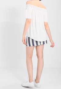 Blusa blanca sin mangas con detalles de encaje, combinada con shorts de mezclilla a rayas. Zapatillas blancas completan el atuendo.
