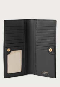 Carteira de couro preto, com múltiplos slots para cartões, uma janela transparente para identificação e um fecho dourado com logótipo em relevo. Textura suave.