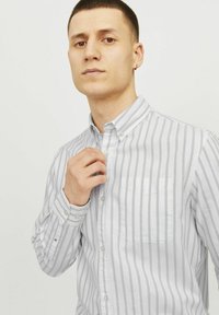 Csíkos ing világosszürke és fehér színben, amely gombos gallérral, egyetlen melltoccsal és hosszú ujjakkal rendelkezik, gombos mandzsettákkal.