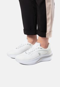 Vita sportskor med perforerat överdel, texturerad design och kontrasterande sula. Har grå accentuer och traditionellt snörsystem.