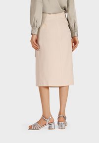 Gonna a matita beige con un design elegante, una texture liscia e un taglio fino al ginocchio, abbinata a sandali con tacco a strappo argentati.