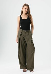 Zwart geribd tanktop gecombineerd met olijfgroene wijde broek met ceintuur en gedrapeerd voorpand. Sandalen met dunne bandjes.