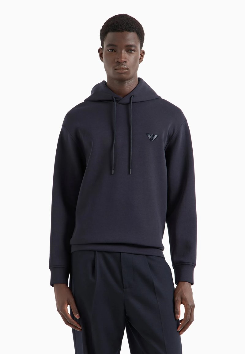 Felpa con cappuccio blu navy in morbido materiale, dotata di tasca a marsupio anteriore, cappuccio con cordino e emblema sul lato sinistro del petto.