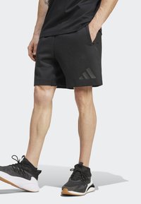 Melnas sporta bikses ar gludu tekstūru, ar sānu kabatām un iecirstu melnu Adidas logo. Kombinētas ar melniem un baltiem sporta apaviem.