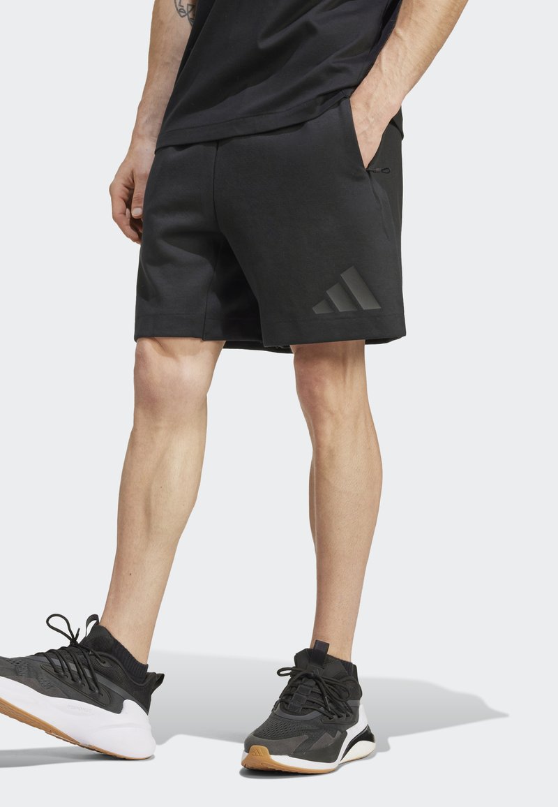 Melnas sporta bikses ar gludu tekstūru, ar sānu kabatām un iecirstu melnu Adidas logo. Kombinētas ar melniem un baltiem sporta apaviem.