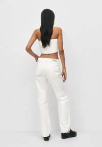 Un top court blanc et un jean large blanc. La tenue présente des lignes épurées, une texture lisse et des éléments de design minimalistes.