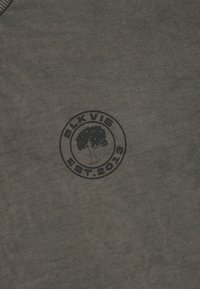 Σκούρο γκρι ύφασμα με μαύρο κυκλικό λογότυπο που περιλαμβάνει ένα δ�έντρο στο κέντρο και την ένδειξη "BLKVIS EST. 2020" γύρω από αυτό.