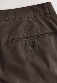Dark brown trousers featuring a back pocket with a button closure, made of smooth fabric with a subtle texture and clean stitching details.