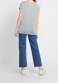 Ljusgrå kortärmad topp med avslappnad passform, tillsammans med blå vida jeans och vita sneakers. Enfärgad, slät textur.