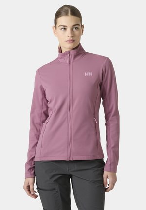 Vrouw draagt een mauve ritsvest met een hoge kraag en het Helly Hansen-logo, gecombineerd met donkergrijze broek, staand tegen een effen achtergrond.