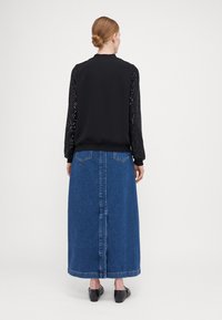 Black top with sequined sleeves, paired with a long blue denim skirt. The outfit features a simple design and a smooth texture. Black shoes complete the look.