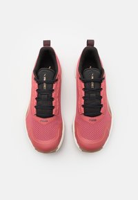 Chaussures de sport avec une tige en mesh texturé rose, des lacets noirs et une semelle rembourrée. Présente des accents dorés et un logo sur le côté.