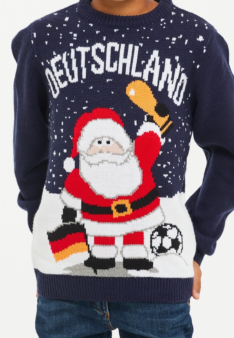 Pull bleu marine avec le Père Noël tenant un trophée et le drapeau allemand, se tenant à côté d’un ballon de football, avec le texte "DEUTSCHLAND" au-dessus.