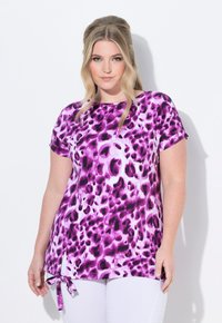 Tričko s krátkým rukávem v purpurovo-bílém leopardím vzoru, kulatým výstřihem, bočními rozparky a detailem na zavazování na spodním lemu. Měkká textilie.