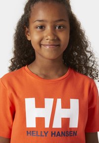 Camiseta de algodón naranja con un logo blanco "HH" y el texto "HELLY HANSEN" en azul marino. Manga corta y un diseño clásico de cuello redondo.