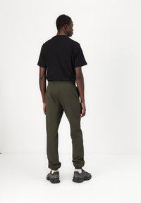 Black short-sleeve t-shirt, olive green sweatpants with elastic cuffs, worn with grey athletic shoes. Clean lines and simple design.