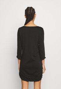 Černé šaty s dlouhými rukávy, lodním výstřihem a řasenými detaily na rukávech a dolním lemu. Vyrobeno z měkké, elastické tkaniny. Přiléhavý střih.