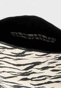 Υφασμάτινη τσάντα με μοτίβο ρίγες ζέβρας σε μαύρο και εκρού χρώμα, κλείσιμο με φερμουάρ και απλή μαύρη εσωτερική επένδυση.