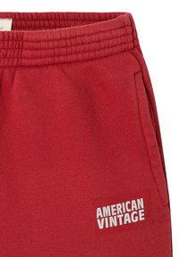 Raudoni medvilniniai sportiniai džinsai su elastingu juosmeniu, su šoninėmis kišenėmis ir baltu logotipu "AMERICAN VINTAGE" kairėje šlaunies pusėje.
