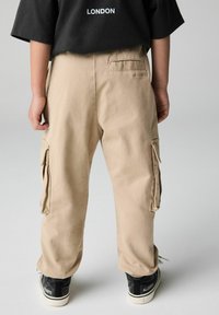 Kaki cargobyxor med sidofickor, lös passform och uppvikta fållar, tillsammans med svarta sneakers. T-shirten har vit text "LONDON" på ryggen.